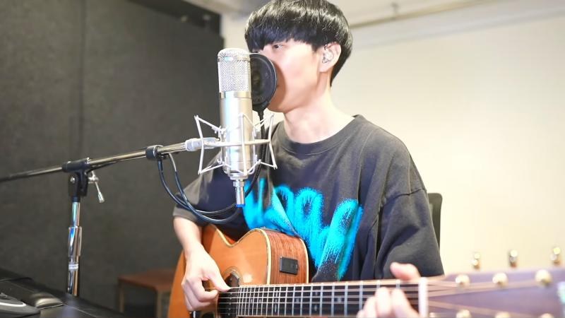 大石昌良さんが大型チューブマイクとアコースティックギターで弾き語りをする様子(YouTube配信より引用)